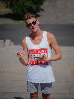 Gülümseyen genç bir adam ile bir limonata kentsel arka plan bulanık. Şık bir adam açık havada güneş gözlüğü. Kopya alanı.