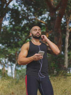 Doğal bir arka planda müzik dinlemek yakışıklı bir erkek. İçinde belgili tanımlık açık havada yürüyen sportif bir adam. Sağlıklı yaşam tarzı.