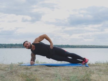 Doğal bir arka plan üzerinde bir mat egzersizleri yapıyor bir kas vücut sportif bir adamla. Spor ve yoga kavramı.