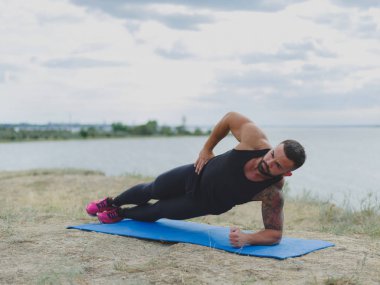 Atletik, güçlü bir adam ile bir kas vücut üzerinde doğal bir arka plan üzerinde bir mat egzersizleri yapıyor. Fitness, spor kavramı.