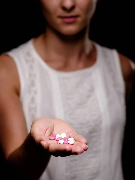 Eine Nahaufnahme eines Tablettenhaufens in weiblicher Hand auf schwarzem Hintergrund. junge Frau mit Tabletten in der Hand. Medizinkonzept. — Stockfoto