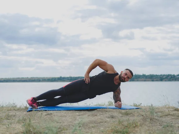 A sportos férfi egy izmos szerv gyakorolja a szőnyegen, a természetes háttér. Sport és jóga koncepció. — Stock Fotó