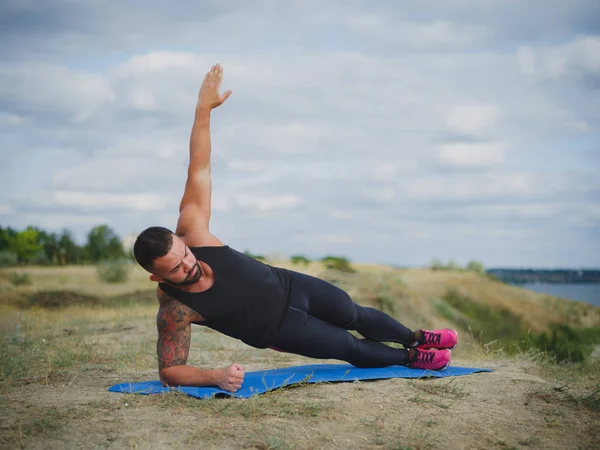 Egy sportos, erős ember gyakorolja a szőnyegen, a természetes háttér izmos test. Fitness, Sport koncepció. — Stock Fotó