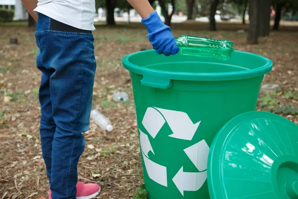 Vücut parçaları. Yakın çekim fotoğraf mavi kot pantolon ve pembe snikers kız çocuğunun mavi lateks eldiven renkli geri dönüşüm üzerinde eller. Plastik torba geri dönüşüm kutusu içine atma el — Stok fotoğraf