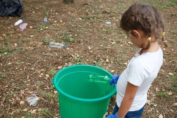 Tyłu miła dziewczyna z warkoczykami fryzurę. Rzucając torebkę do recyklingu bin. Gruntów i śmieci na tle. — Zdjęcie stockowe