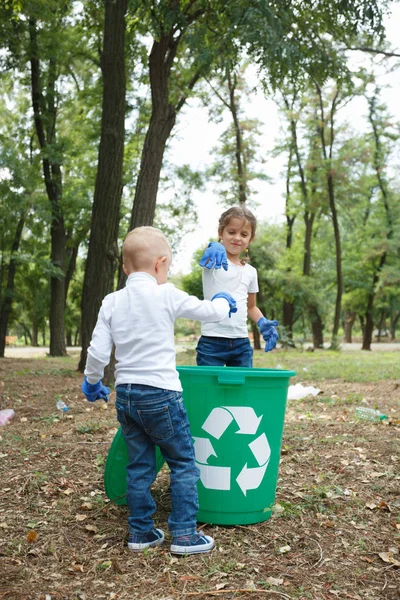 Tyłu Targi chłopiec z fryzura warkocze. Rzucając torebkę do recyklingu bin. Gruntów i śmieci na tle. — Zdjęcie stockowe