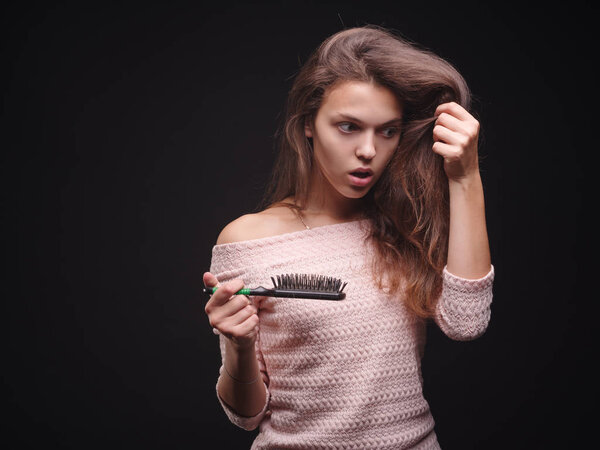 Stressed woman with hair problems on a black background. Vitamins for fragile hair. Hair treatment concept. Copy space.