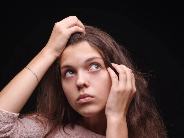 Stressed woman with hair problems on a black background. Vitamins for fragile hair. Hair treatment concept. Copy space.