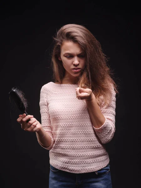 Stressed woman with hair problems on a black background. Vitamins for fragile hair. Hair treatment concept. Copy space.