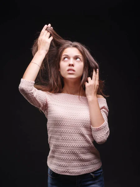 Шокована жінка тягне своє хворобливе волосся на чорному тлі. Чудова жінка незадоволена волоссям. Концепція рутинного волосся . — стокове фото