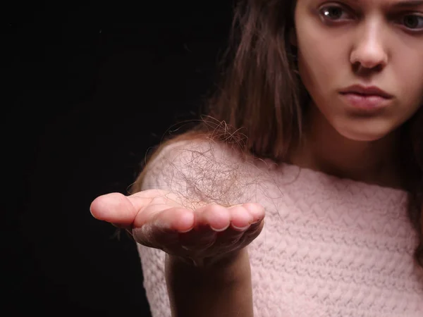 Close-up tuft of hair on a hand. Sad woman holding tangled hair on the black background. Hair loss concept. Copy space.