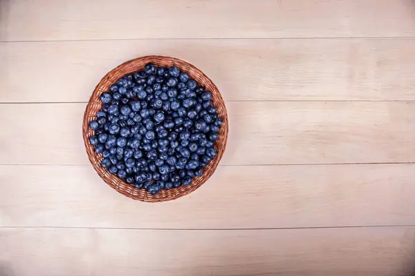 Una canasta de arándanos sobre un fondo de madera clara. Hermosos arándanos en una canasta. Bayas vegetarianas saludables. Copiar espacio . — Foto de Stock