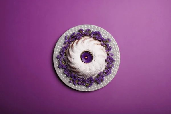 Вид сверху кольцевого торта, посыпанного сахарной пудрой, с фиолетовой свечой в центре на ярко-фиолетовом фоне . — стоковое фото