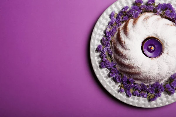 Тарелка с круглым тортом посыпанным сахарной пудрой и свечой в центре на ярком фиолетовом фоне, вид сверху . — стоковое фото