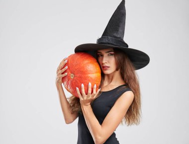 Şapkalı, güzel, sihirli cadı kız balkabağına gri bir arka plan üzerinde tutarak. Cadılar Bayramı kavramı.