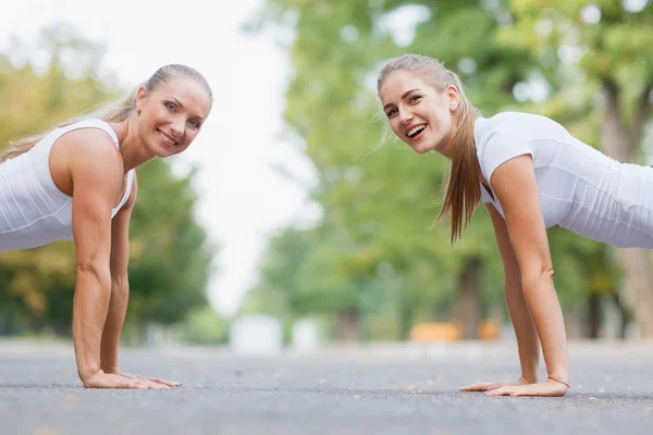 Chicas de fitness haciendo flexiones al aire libre en un fondo del parque. Chicas deportivas. Concepto de entrenamiento. Copiar espacio . — Foto de Stock
