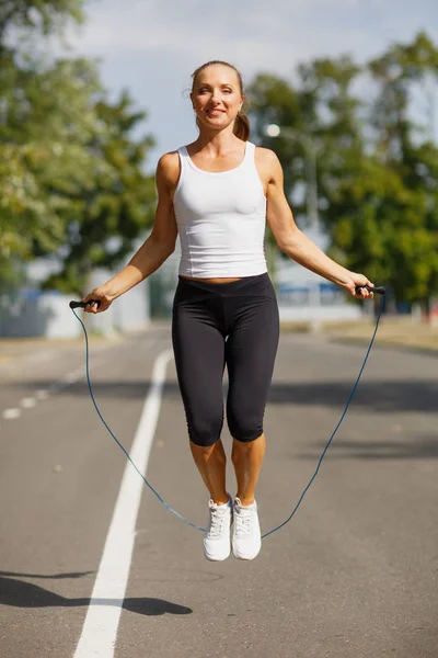 Beautiful girl with a jumping rope. Sports woman jumping on a park background. Active lifestyle concept.