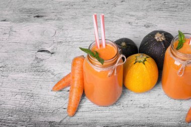 İki uzun boylu şişe ile bir vejetaryen güler yüzlü tatlı havuç, sağlıklı kabakları, nane yaprakları ve gri bir ahşap zemin üzerine süslü çöp. Organik, rustik malzemeler güzel dizi Gurmeler için.