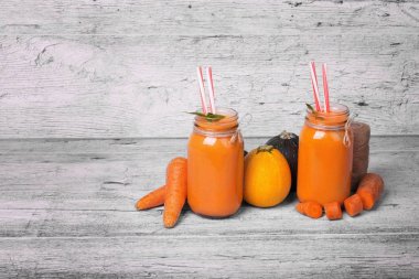 İki uzun boylu şişe ile bir vejetaryen güler yüzlü tatlı havuç, sağlıklı kabakları, nane yaprakları ve gri bir ahşap zemin üzerine süslü çöp. Gurmeler için organik, rustik malzemeler. Kopya alanı.