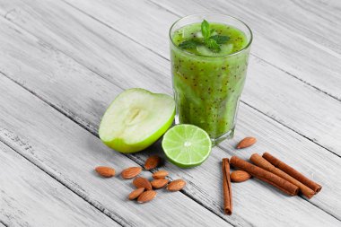 Kivi, elma ve kireç organik içki dolu bir cam üstten görünüm gri bir ahşap zemin üzerinde. Yeşil elma ve Ekşi limon bir masa üzerine ikiye böldüm. Tarçın ve badem yakınındaki bir kompozisyon.