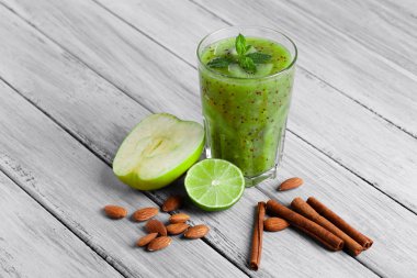 Kivi, elma ve kireç organik içki dolu bir cam üstten görünüm gri bir ahşap zemin üzerinde. Yeşil elma ve Ekşi limon bir masa üzerine ikiye böldüm. Tarçın ve badem yakınındaki bir kompozisyon.