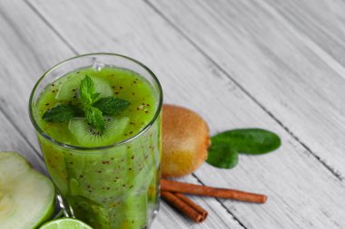 Bir bardak tatlı kivi, elma ve gri bir ahşap zemin üzerine yeşil nane kokteyl serinletici tam bir görünümünü yukarıda. Baharatlı tarçın, meyveli içecek yakınındaki Bütün Konfit kivi. Kopya alanı.