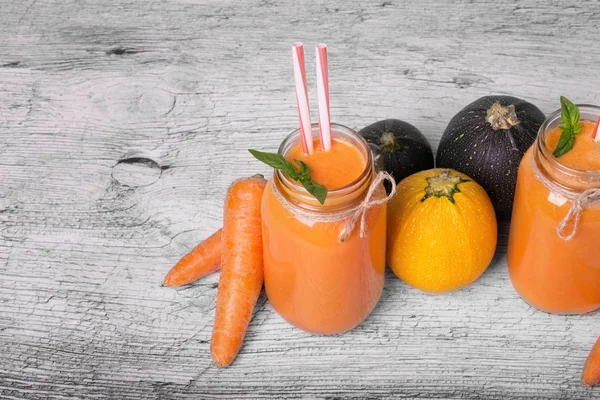 İki uzun boylu şişe ile bir vejetaryen güler yüzlü tatlı havuç, sağlıklı kabakları, nane yaprakları ve gri bir ahşap zemin üzerine süslü çöp. Organik, rustik malzemeler güzel dizi Gurmeler için.