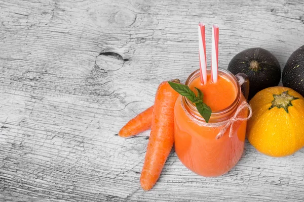 Ferah ışık gri arka plan üzerinde Besleyici bir sebze içecek bir cam şişe. Soyulmuş havuç ve çok renkli kabakları bir tablo. Kahvaltı için taze nane ile portakal suyu. Kopya alanı.