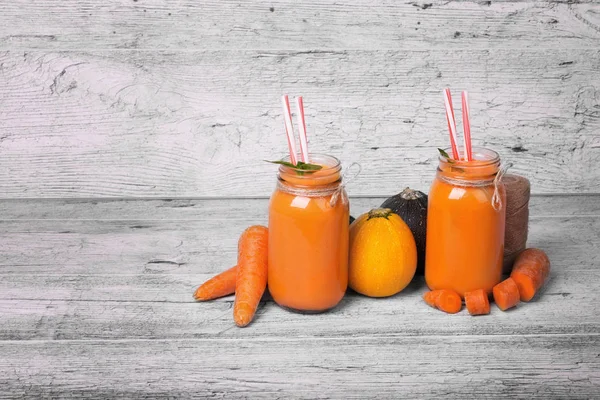 İki uzun boylu şişe ile bir vejetaryen güler yüzlü tatlı havuç, sağlıklı kabakları, nane yaprakları ve gri bir ahşap zemin üzerine süslü çöp. Gurmeler için organik, rustik malzemeler. Kopya alanı.