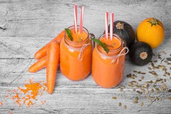 İki uzun boylu şişe ile bir vejetaryen güler yüzlü tatlı havuç, sağlıklı kabakları, nane yaprakları ve gri bir ahşap zemin üzerinde kabak çekirdeği. Organik, rustik malzemeler güzel dizi Gurmeler için.