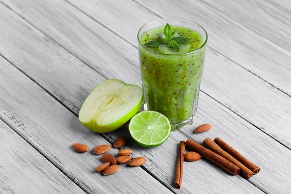 Kivi, elma ve kireç organik içki dolu bir cam üstten görünüm gri bir ahşap zemin üzerinde. Yeşil elma ve Ekşi limon bir masa üzerine ikiye böldüm. Tarçın ve badem yakınındaki bir kompozisyon.