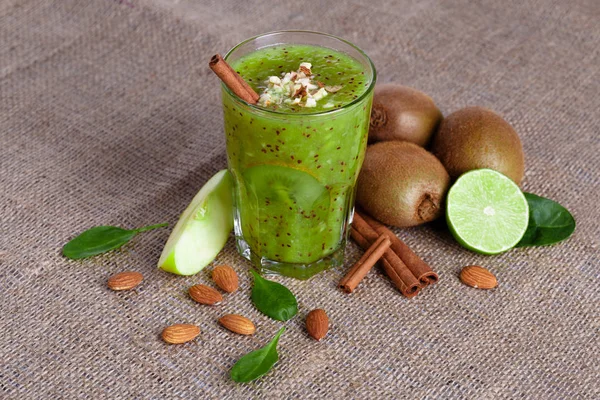 Hafif kahverengi kumaş arka plan üzerinde Sulu kireç, tatlı kivi ve elma yığını bir manzara yukarıdan. Tarçın, badem ve masada yeşil yaprakları. Besleyici vitamin meyveli kokteyl dolu.