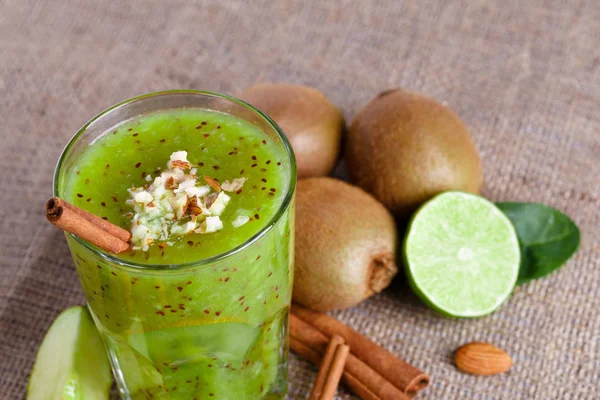 Yakın çekim olgun kivi ve rendelenmiş badem ve tarçın hafif kahverengi kumaş arka plan üzerinde limonlu karışık bir içki. Bir kaç bütün sulu kivi, limon da pay yarım ve bir masa üzerine elma dilim.