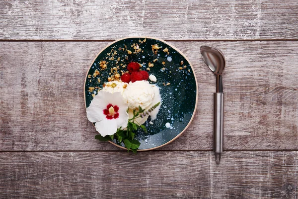 Κάτοψη του ένα παγωτό βανίλια σε ένα πιάτο και μια σέσουλα. Παγωτό με ένα λουλούδι. Γλυκό επιδόρπιο σε ένα ξύλινο υπόβαθρο. Χώρο αντίγραφο. — Φωτογραφία Αρχείου