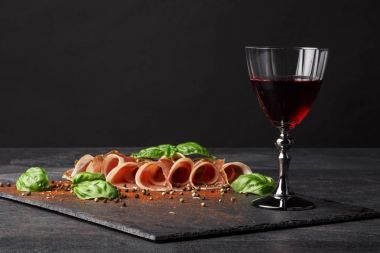 İnce dilimlenmiş aşağıdaki ve doygun siyah zemin üzerine kırmızı şarap. Kuru kırmızı şarap, geleneksel İtalyan aperatifleri, fesleğen ve karabiber masanın üzerinde. Kopya alanı.