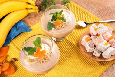 Bir tablo ile bir tabak tatlı Türk Lokumu, Kuru Kayısı, ceviz, metalik bir kaşık, parlak sarı muz, renkli arka plan üzerinde bir kokteylle iki bardak.