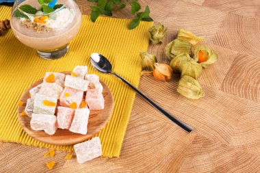 Klasik Türk Lokumu, kalın muzlu kokteyl büyük bir cam ve tropikal physalis meyve dekoratif sarı kumaş bir ahşap Resepsiyon arka plan üzerinde renkli bir ışık kümesi. Besleyici sağlıklı atıştırmalıklar.