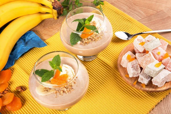 Bir tablo ile bir tabak tatlı Türk Lokumu, Kuru Kayısı, ceviz, metalik bir kaşık, parlak sarı muz, renkli arka plan üzerinde bir kokteylle iki bardak.