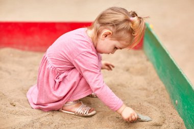 Bir kum içinde pembe elbiseli küçük kız.