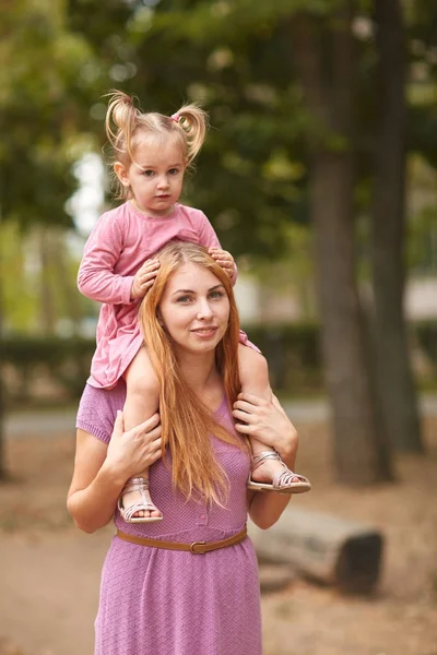 A filha senta-se em meus ombros de mães em um vestido rosa . — Fotografia de Stock