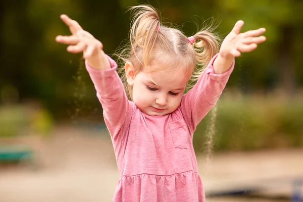 Klein meisje in roze jurk spelen met zand — Stockfoto