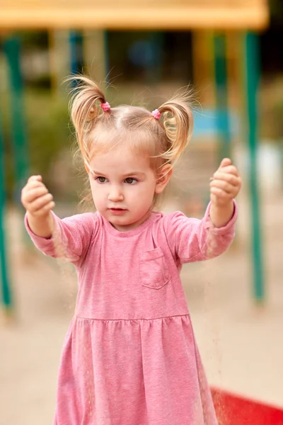 Kleines Mädchen im rosa Kleid spielt mit Sand — Stockfoto