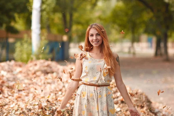 Rudowłosa dziewczyna w białej sukni tosss liści w parku — Zdjęcie stockowe
