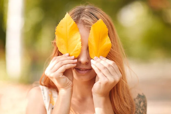 Kızıl saçlı kız sonbahar yaprakları ile gözlerini kapatır — Stok fotoğraf