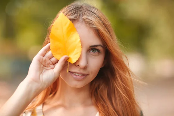 Kızıl saçlı kız sonbahar yaprakları ile gözlerini kapatır — Stok fotoğraf