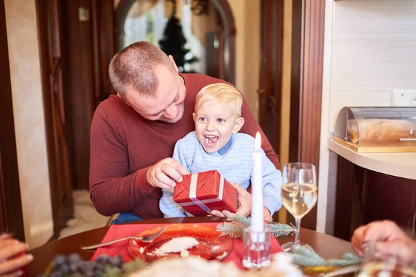 Dad giving a red gift to little son on a festive background. Family Christmas presents concept. — Stock Photo, Image