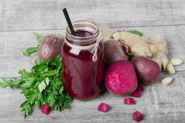 Bir büyük mason kavanoza pancar suyu ile siyah saman dolu güzel bir kompozisyon üstten görünüm gri bir ahşap zemin üzerinde. Bütün ve kesme kırmızı pancar, taze yeşil maydanoz ve zencefil masada.