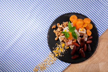 Siyah plaka yummies ve meyve dolu bir üstten görünüm renkli kumaş arka plan üzerinde. Kırmızı tarihi meyve, aromatik nane, Kuru Kayısı ve gevrek ceviz ile şekerli Türk lokumu. Kopya alanı.