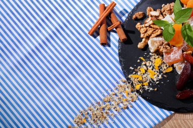 Çizgili Kumaş arka plan üzerinde bir tabakta üstten görünüm besleyici şekerlemeler maddeler. Hafif kahverengi ceviz, taze nane ve tarçın ile pudra şekeri Türk lokumu. Kopya alanı.