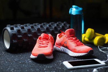 Mavi bir şişe su, sarı dambıl, kulaklık ve pembe canlı koşu ayakkabıları spor rutin olarak karanlık bir arka plan bulanık için beyaz bir cep telefonuyla için.